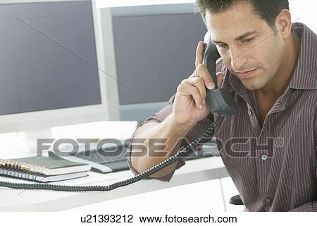 Stock Image - Businessman using telephone at desk in office. Fotosearch