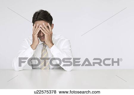 Stock Photo - Businessman with head in hands at table. Fotosearch