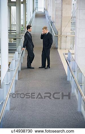 Stock Image - Businessmen in office building hallway. Fotosearch