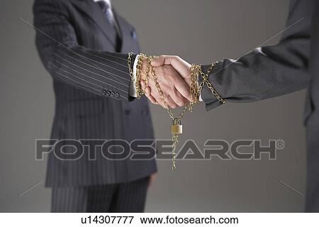 Businessmen shaking hands wrapped in gold chain with padlock, mid section View Large Photo Image Stock Photo - Businessmen shaking hands wrapped in gold chain with padlock, mid section. Fotosearch