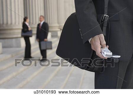Stock Image - Businessmen Using Cell Phone and People Talking in Background. Fotosearch