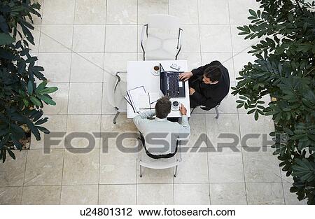Stock Image - Businessmen using laptop at outdoor table, view from above. Fotosearch