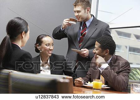 Stock Image - Businesspeople in eating and drinking in board room. Fotosearch