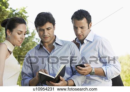 Stock Image - Businesspeople looking at diary in park. Fotosearch