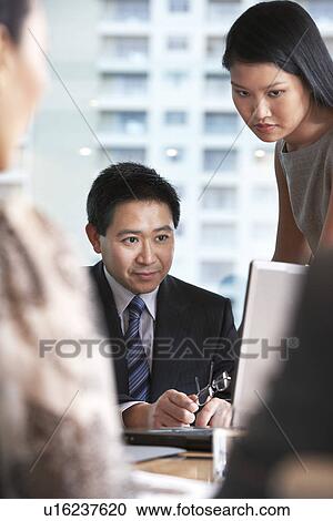 Stock Image - Businesspeople looking at laptop screen in office. Fotosearch