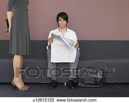 Stock Image - Businesswoman and Businessman Reading Newspaper in Lobby. Fotosearch