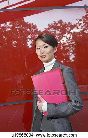 Businesswoman holding notebook, Standing Beside red Building View Large Photo Image Picture - Businesswoman holding notebook, Standing Beside red Building. Fotosearch