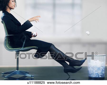 Stock Photography - Businesswoman sitting in chair throwing balls of paper into waste basket. Fotosearch