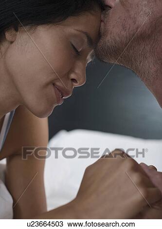 Stock Image - Close-up of mid-adult man kissing his girlfriend's forehead. Fotosearch