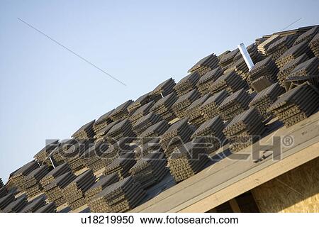 Stock Image - Close-up view of stacks of roof tiles on roof, construction site. Fotosearch