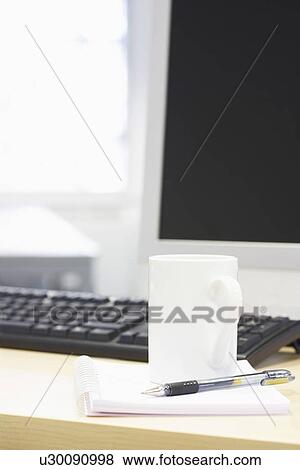 Stock Photo - Coffee mug and pen on desk by computer, close up. Fotosearch