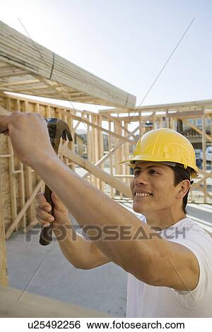 Construction worker hammering on construction site View Large Photo Image Stock Photograph - Construction worker hammering on construction site. Fotosearch