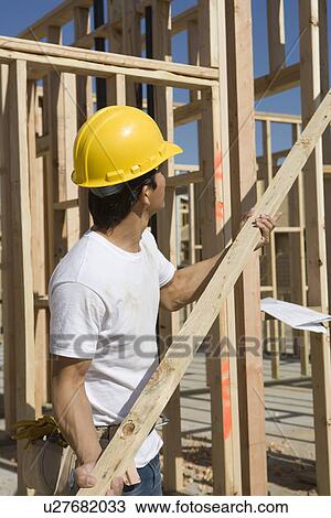 Stock Image - Construction worker holding plank. Fotosearch