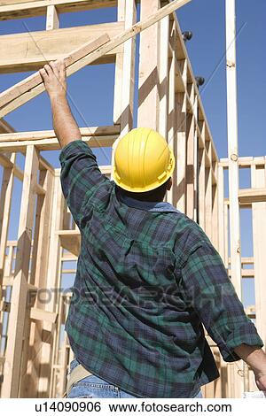 Stock Photograph - Construction worker holding planks, back view. Fotosearch