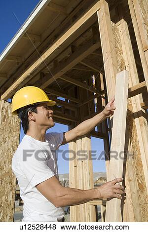 Stock Photo - Construction worker holding wooden beam. Fotosearch