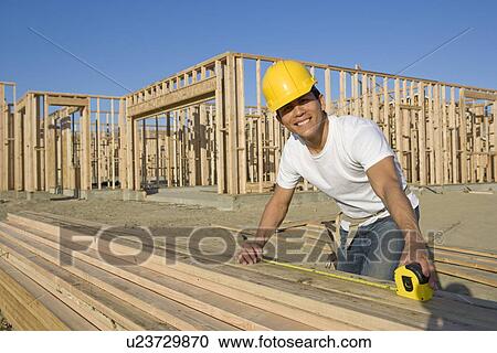 Stock Image - Construction worker measuring wooden planks. Fotosearch