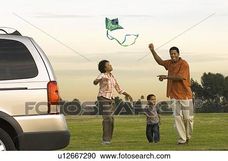 Stock Image - Couple and young son flying kite by car in park. Fotosearch