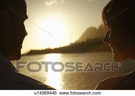 Stock Photograph - Couple by lake at sunset, close-up back view.. Fotosearch