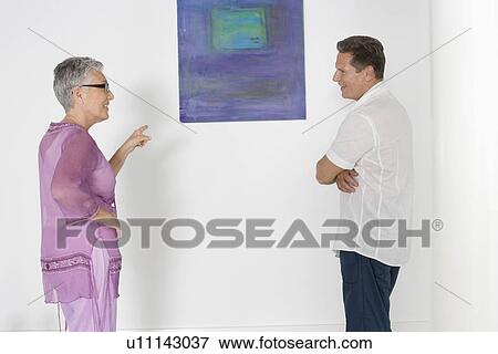 Stock Photo - Couple contemplating paintings in gallery. Fotosearch