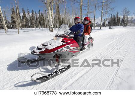 Couple driving snowmobile on snow covered track View Large Photo Image Stock Photo - Couple driving snowmobile on snow covered track. Fotosearch