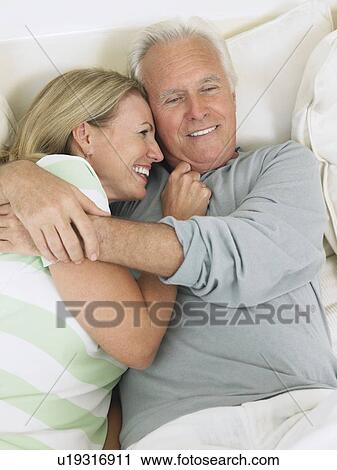 Stock Image - Couple embracing, lying on bed, elevated view. Fotosearch