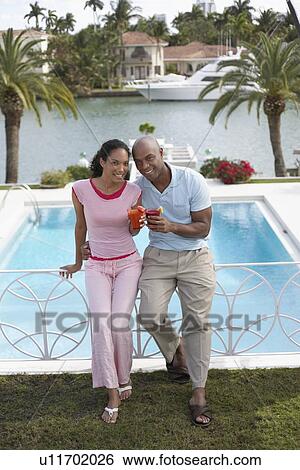 Couple holding cocktails leaning on pool banister View Large Photo Image Stock Photograph - Couple holding cocktails leaning on pool banister. Fotosearch