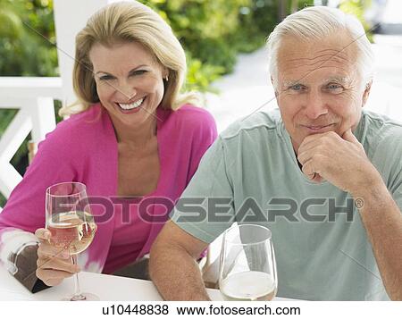 Couple holding wine glasses, sitting at verandah table, elevated view View Large Photo Image Stock Photo - Couple holding wine glasses, sitting at verandah table, elevated view. Fotosearch