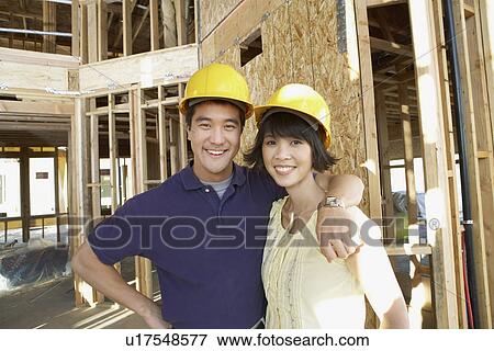 Couple in hard hats in front of house being built View Large Photo Image Stock Photo - Couple in hard hats in front of house being built. Fotosearch