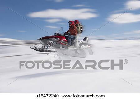 Stock Image - Couple jumping snowmobile in snow, mid air. Fotosearch