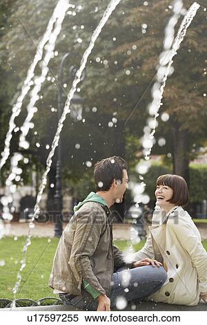 Couple laughing sitting on edge of fountain, view past water jets View Large Photo Image Stock Photography - Couple laughing sitting on edge of fountain, view past water jets. Fotosearch