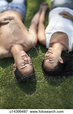 Stock Photo - Couple listening to mp3 player lying down side by side on park lawn, elevated. Fotosearch