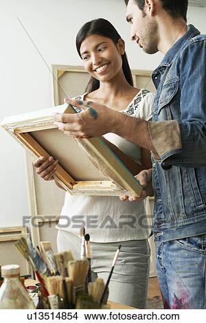 Picture - Couple looking at canvases in artist studio. Fotosearch