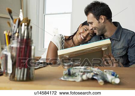 Stock Image - Couple looking at painting in artist studio. Fotosearch