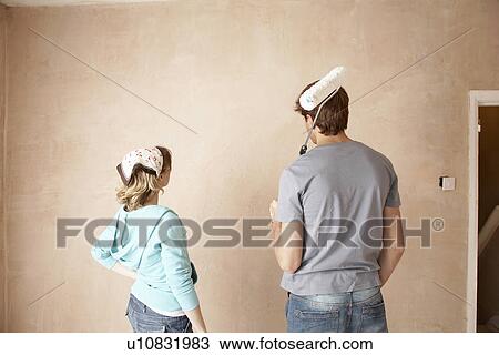 Stock Image - Couple looking at wall of unrenovated room, back view. Fotosearch