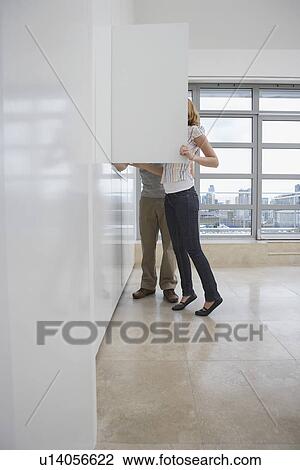 Stock Image - Couple looking in cupboard in empty apartment. Fotosearch