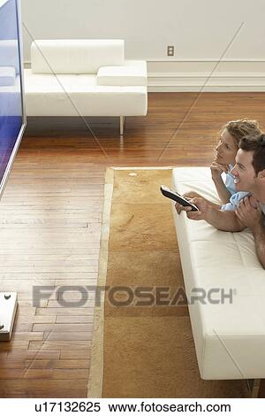 Stock Photography - Couple lying on bed, watching plasma TV together. Fotosearch