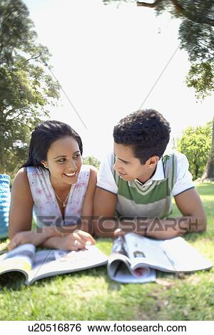 Stock Photograph - Couple lying on grass reading magazines. Fotosearch
