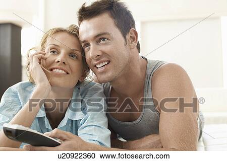 Couple on bed watching television, man holding remote control View Large Photo Image Stock Image - Couple on bed watching television, man holding remote control. Fotosearch