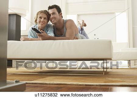 Couple on bed watching television together, man holding remote control View Large Photo Image Stock Image - Couple on bed watching television together, man holding remote control. Fotosearch