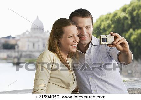 Stock Image - Couple photographing selves on bridge in Rome, Italy, front view. Fotosearch