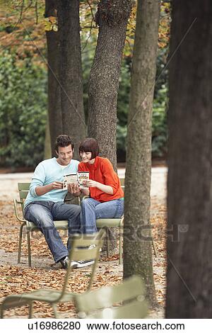 Stock Image - Couple reading guide book, sitting on chairs, in park. Fotosearch