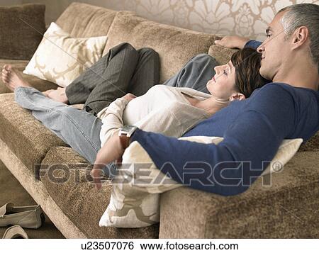 Couple relaxing on sofa in living room View Large Photo Image Stock Photograph - Couple relaxing on sofa in living room. Fotosearch
