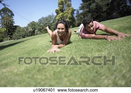 Stock Image - Couple rolling on grass in park. Fotosearch