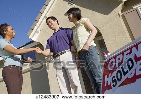 Stock Photo - Couple shaking hands with estate agent outside their new home. Fotosearch