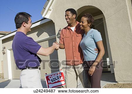 Couple shaking hands with estate agent outside their new home View Large Photo Image Stock Photo - Couple shaking hands with estate agent outside their new home. Fotosearch