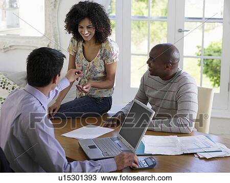 Stock Image - Couple sitting at dining table with financial advisor, elevated view. Fotosearch