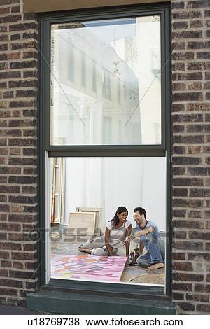 Couple sitting by painting on floor of artist studio, view through window View Large Photo Image Stock Photo - Couple sitting by painting on floor of artist studio, view through window. Fotosearch