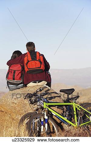 Couple sitting on boulder, mountain bikes in foreground, back view. View Large Photo Image Stock Photo - Couple sitting on boulder, mountain bikes in foreground, back view.. Fotosearch