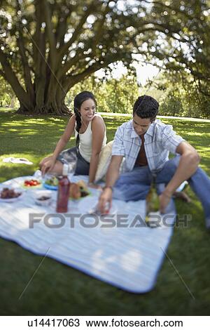 Stock Image - Couple sitting on picnic blanket in park. Fotosearch