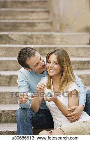 Stock Image - Couple sitting on steps Eating Gelato, front view. Fotosearch